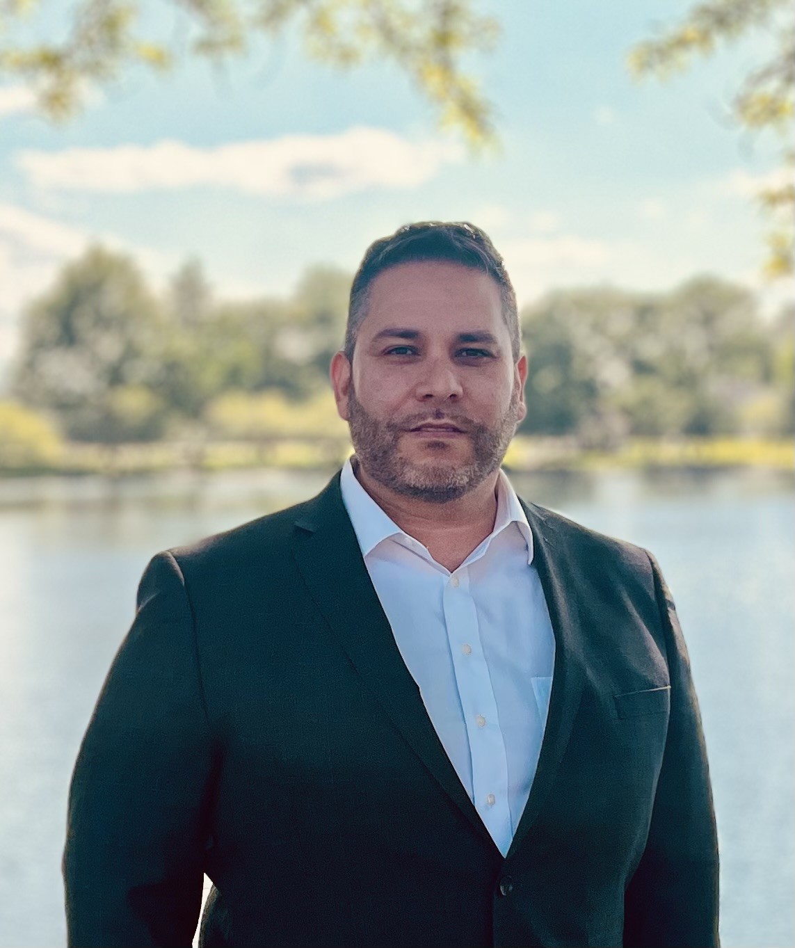 Gil Gonzales - photo from the chest up in a gray suit jacket with the lake in the background.