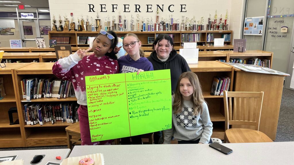 6th grade students in Limitless Ambition, Spring 2024 4 Barberton students standing in the library with a handmade sign listing "unhealthy" and "healthy" behavior.
